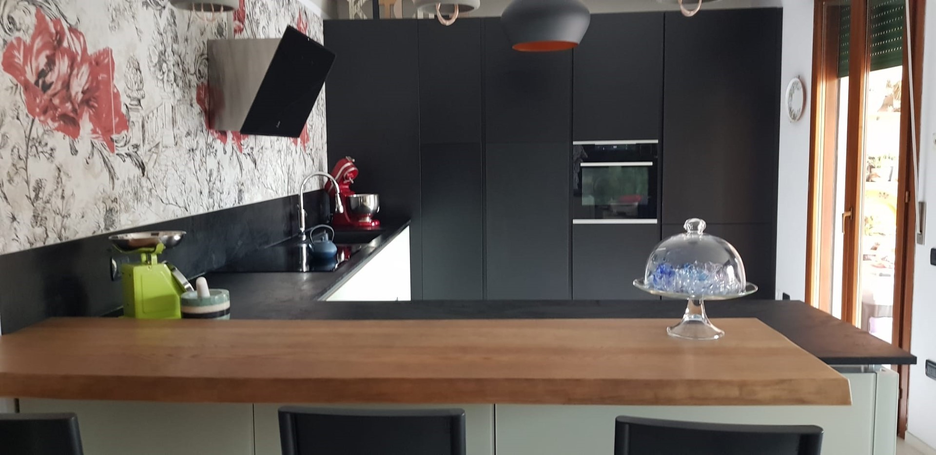Zona cucina arredata con pianali ed arredamenti di colore nero con murale floreale bianco e rosso.